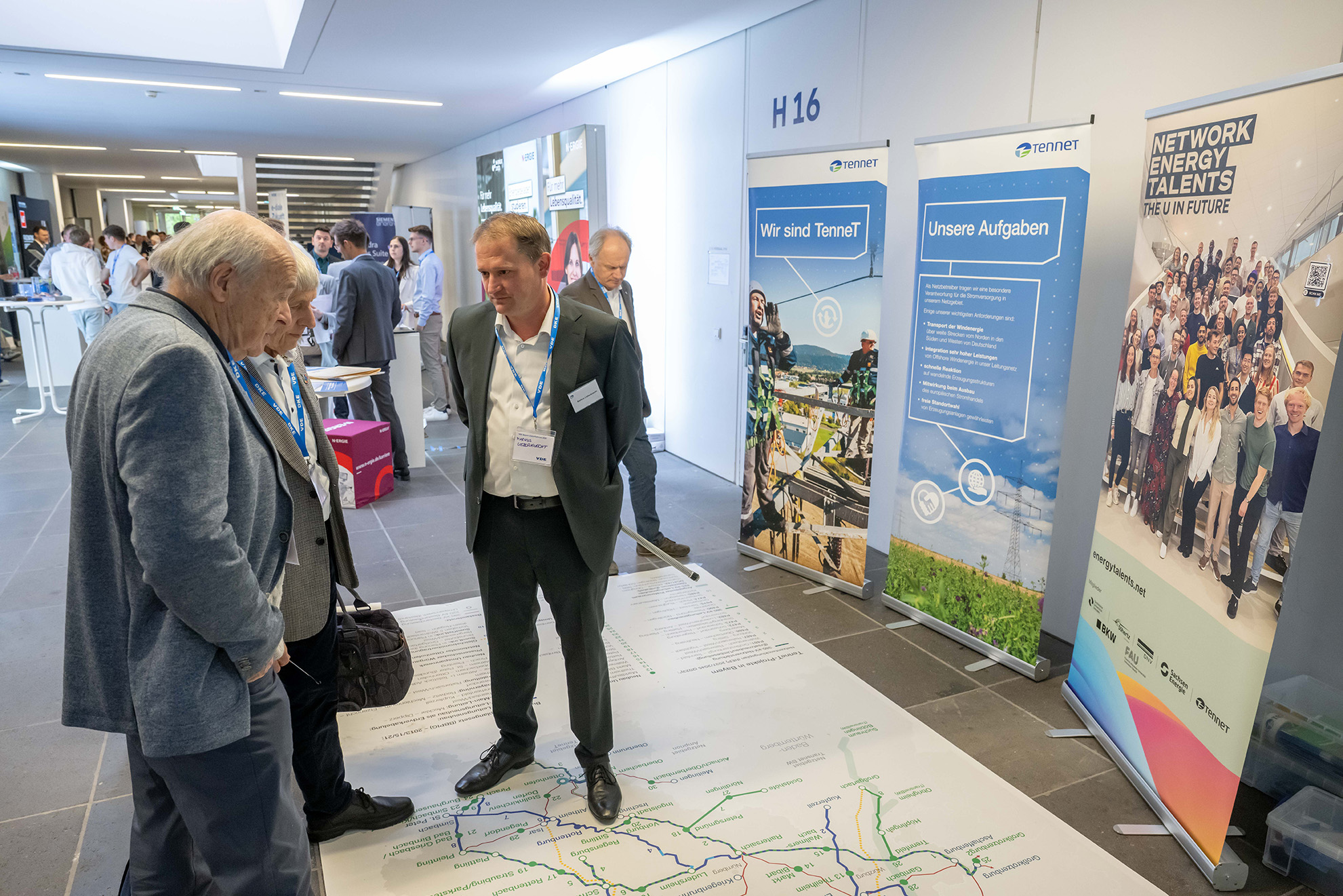 Gespräch am NET- und TenneT-Stand mit großer Bodenkarte auf einer Veranstaltung.