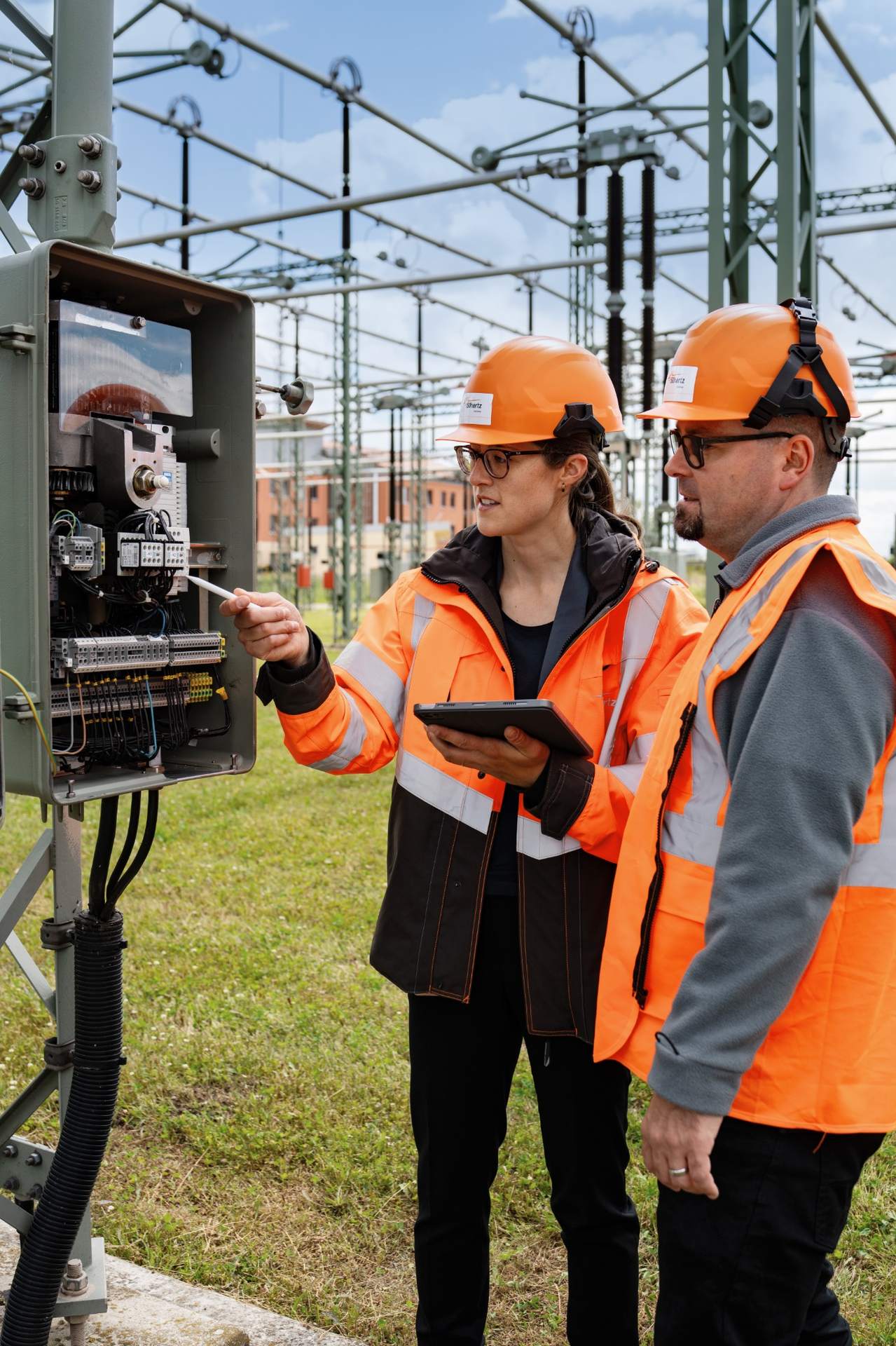 Two 50Hertz employees inspect technical equipment at a substation.