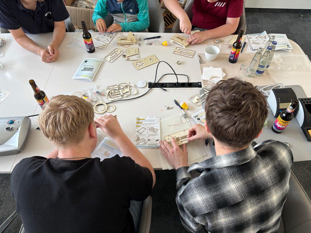 Jugendliche bauen an einem Tisch Mini-Generatoren mit Bauteilen und Anleitungen