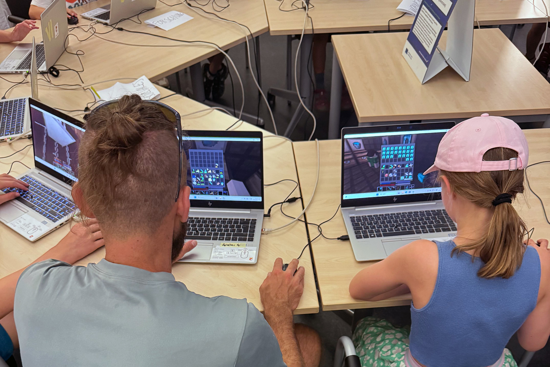 Schüler und Betreuer arbeiten gemeinsam an Laptops im digitalen Newtopia-Spiel