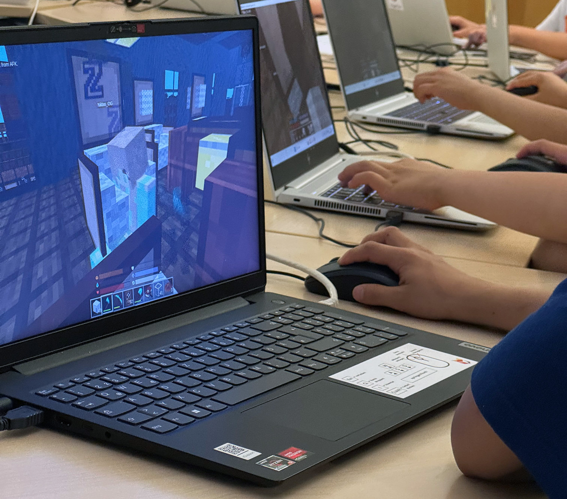 Nahaufnahme mehrerer Laptops mit Newtopia-Spiel und arbeitenden Kinderhänden