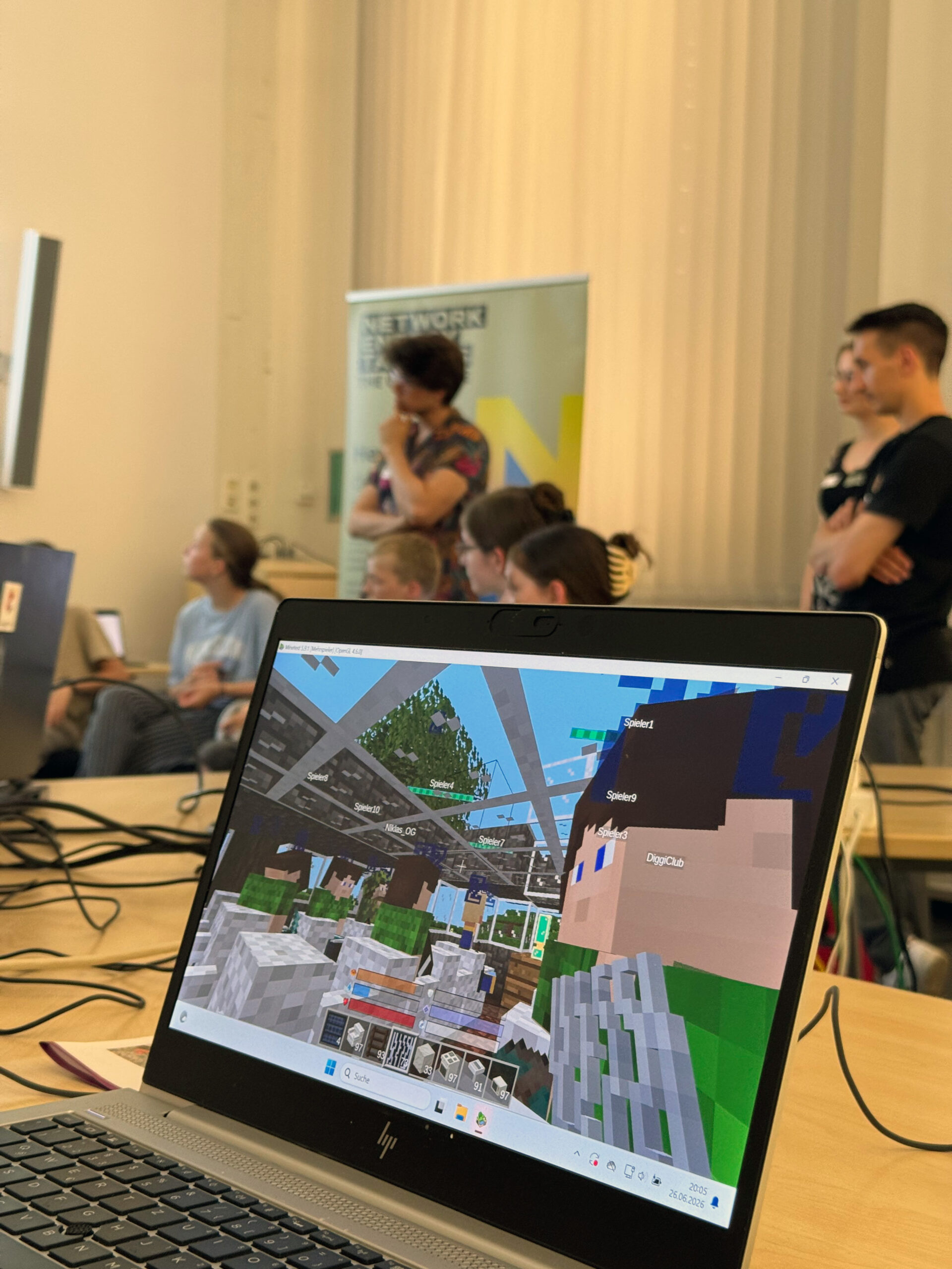 Laptop zeigt Newtopia-Spiel, während Kinder im Hintergrund der Einführung folgen