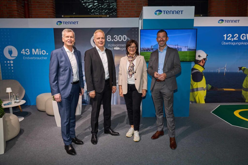 Vier Personen stehen gemeinsam vor einem Messestand von TenneT.
