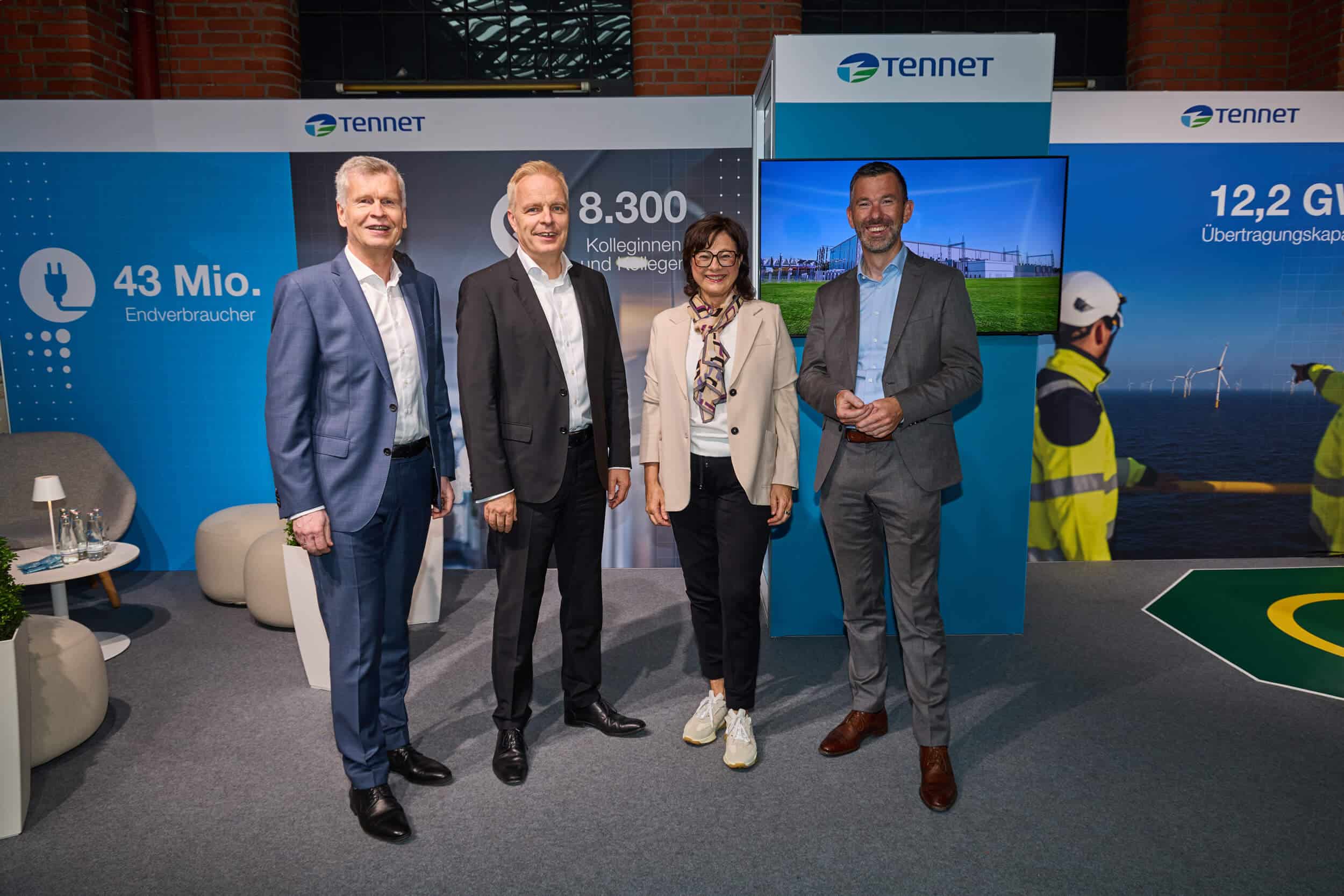 Vier Personen stehen gemeinsam vor einem Messestand von TenneT.