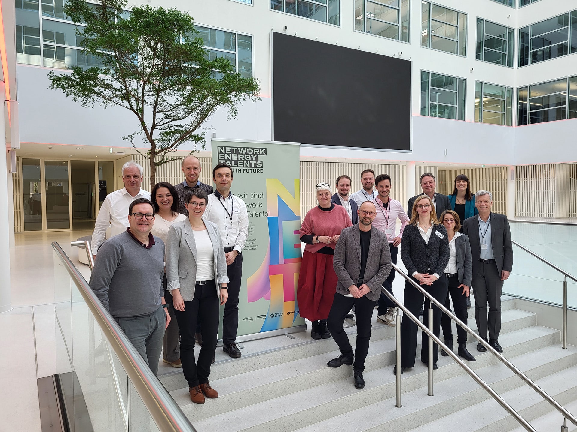 Gruppe vor NET-Banner in modernem Gebäude, Teamfoto auf Treppe im Innenraum