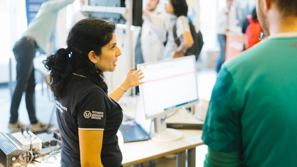Frau erklärt einem Besucher eine technische Anwendung an einem Messestand