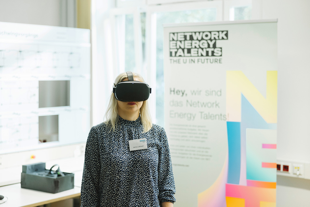 Person mit VR-Brille vor Network Energy Talents Roll-up und Präsentationsscreen