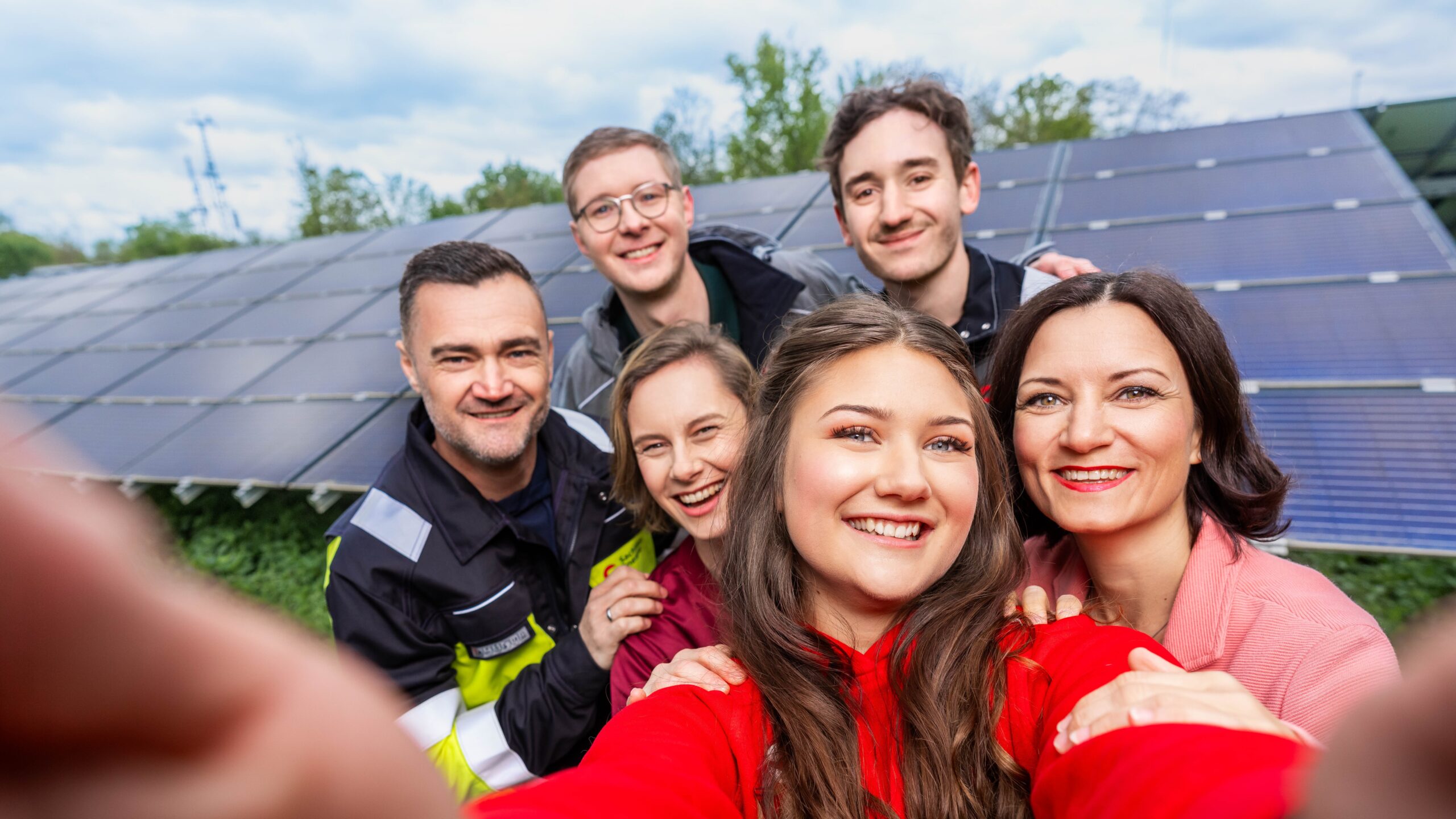Sechs Personen machen gemeinsam ein Selfie vor einer Photovoltaikanlage.