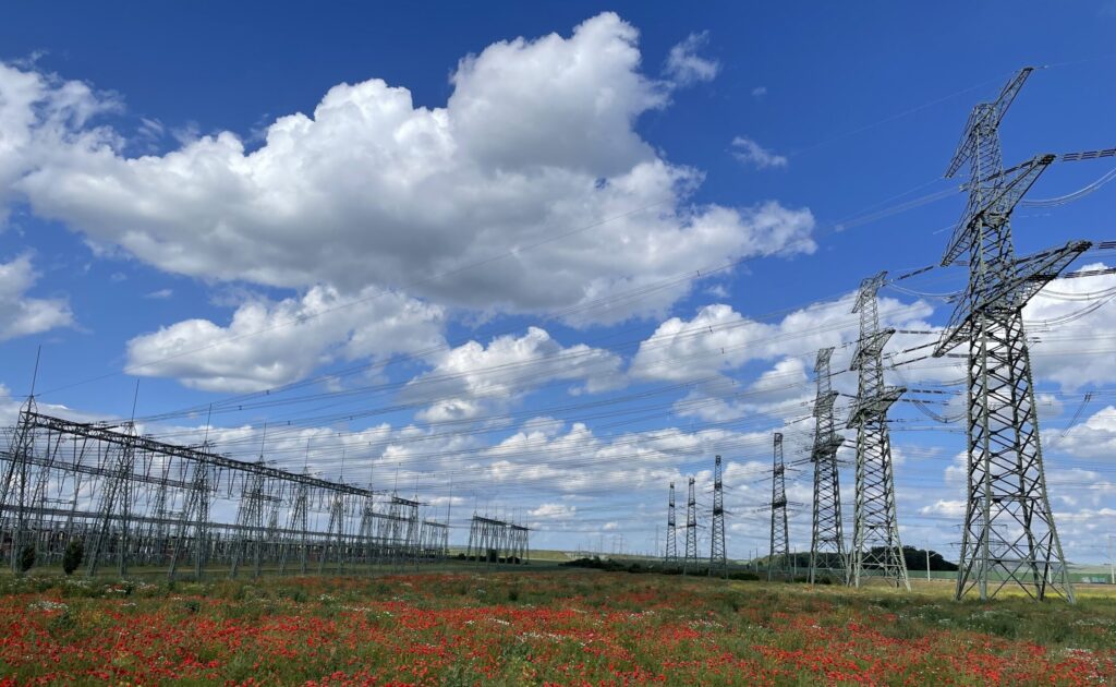 Umspannwerk mit Hochspannungsmasten und Stromleitungen unter blauem Himmel.